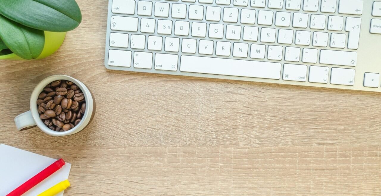 Overhead view of keyboard, coffee beans, and stationery on a wooden desk. Rappresentazione di chiarezza e trasparenza editoriale
