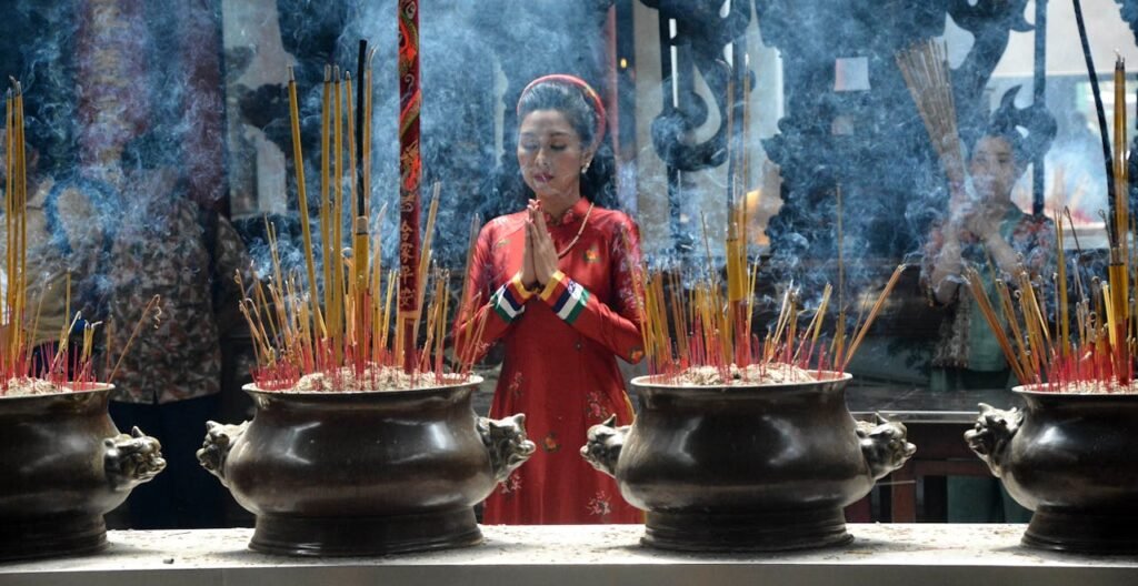 Immagine che illustra antichi rituali di una donna vietnamita in preghiera, avvolta da nuvole di incenso proveniente da stick in vasi cerimoniali